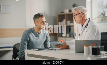 Medico di famiglia di mezza età con esperienza che mostra i risultati dell'analisi sul computer tablet al paziente maschio durante la consultazione in una clinica sanitaria. Medico seduto dietro una scrivania nello studio ospedaliero. Foto Stock