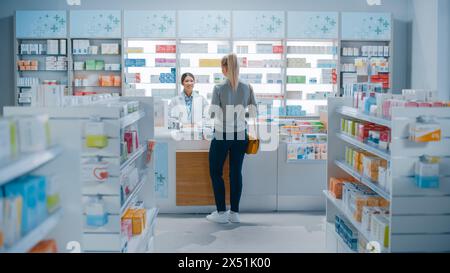 Farmacia farmacia: Bella giovane donna che acquista medicina, farmaci, vitamine si trova accanto al banco cassa. Cassiera femminile in cappotto bianco al servizio del cliente. Scaffali con prodotti sanitari Foto Stock