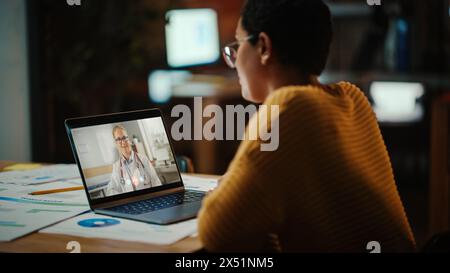 Il bellissimo multietnico Latina Manager sta effettuando una videochiamata al suo medico su un laptop in un ambiente ufficio creativo. L'uomo sta parlando con il suo consulente medico su una telecamera dal vivo, chiedendo di salute. Foto Stock