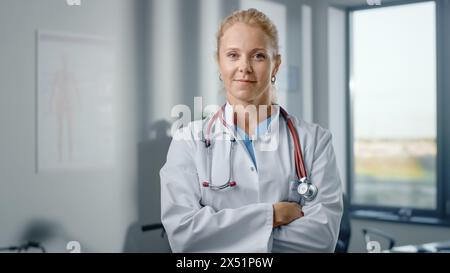 Primo piano Ritratto di bella donna Caucasica medico professionista in piedi nel suo ufficio della clinica di salute. Eroe medico di successo e sicuro guarda la telecamera, sorride in ospedale Foto Stock