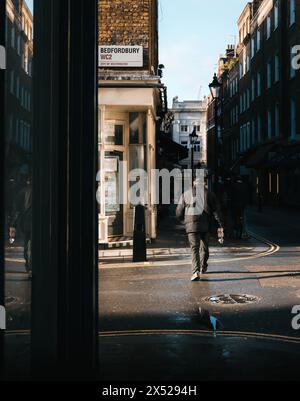 Foto di strada di Man Crossing Street alla luce del sole del mattino con Dark Shadows a Londra, Regno Unito Foto Stock