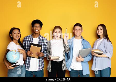 Gruppo di studenti diversi che tengono materiale didattico su sfondo giallo Foto Stock