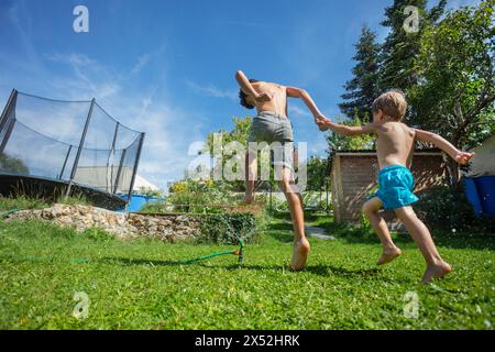 Due ragazzi giocosi si divertono a giocare in acqua nel cortile erboso di casa Foto Stock