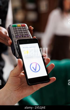 Vista dettagliata del concierge che aiuta anziani pensionati a pagare utilizzando il cellulare e la tecnologia NFC. Primo piano di un viaggiatore che paga con un dispositivo mobile con l'assistenza di un dipendente dell'hotel. Foto Stock