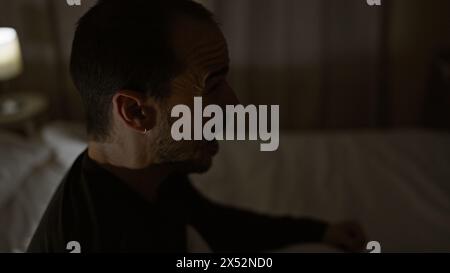 Una vista del profilo di un uomo calvo pensivo con la barba in una stanza poco illuminata di notte, che trasmette un'atmosfera tranquilla. Foto Stock