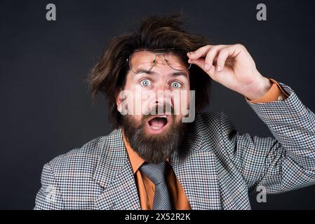 Ritratto di un uomo d'affari confuso con la barba che si toglie gli occhiali. Scioccante uomo barbuto in tuta che tolgono gli occhiali da vista. Uomo d'affari frustrato e alla moda Foto Stock