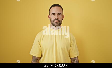 Ritratto di un giovane ispanico sicuro di sé con barba e tatuaggi su sfondo giallo. Foto Stock