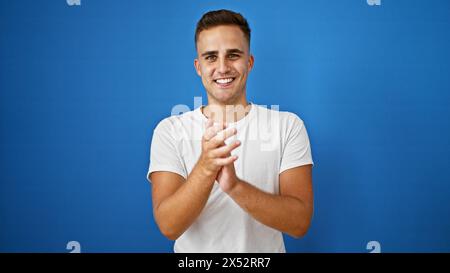 Un giovane allegro che batte le mani su uno sfondo blu intenso e isolato, incarnando gioia e positività. Foto Stock