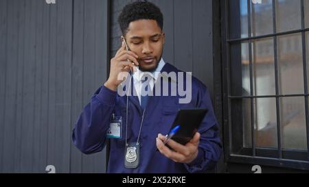 Ufficiale delle forze dell'ordine afroamericane in uniforme che usa lo smartphone e parla al telefono sullo sfondo urbano Foto Stock