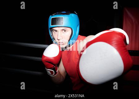 Giovane pugile maschio che colpisce il suo rivale con la mano sinistra in un guanto da boxe e mantiene la difesa di uno a destra durante il combattimento di sparring sull'anello di boxe Foto Stock