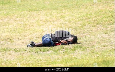 Senzatetto nero africano sdraiato sull'erba concetto di sonno difficoltà economiche o tempi duri in Sud Africa con spazio di copia Foto Stock