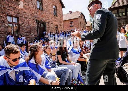 Un militare israeliano parla ai giovani israeliani mentre arrivano per la marcia dei vivi 2024 al campo di Auschwitz. I sopravvissuti all'Olocausto e i sopravvissuti del 7 ottobre partecipano alla marcia dei vivi insieme ad una delegazione di Stati Uniti, Canada, Italia, Regno Unito. Durante il Memorial Day dell'Olocausto osservato nel calendario ebraico (Yom HaShoah), migliaia di partecipanti marciano silenziosamente da Auschwitz a Birkenau. La marcia ha uno scopo educativo e commemorativo. La marcia di quest'anno è stata altamente politicizzata a causa della guerra israeliana nella Palestina occupata. Foto Stock