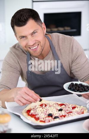 uomo che aggiunge olive a una pizza fatta in casa Foto Stock