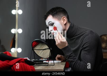 Giovane che applica il trucco mimo vicino allo specchio nello spogliatoio Foto Stock