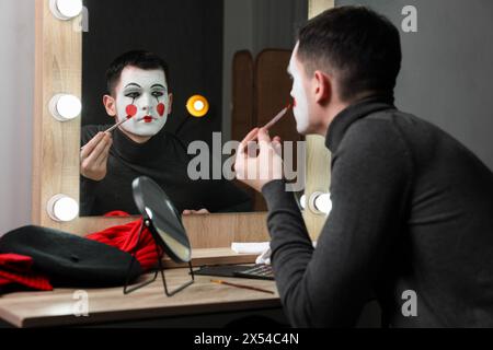 Giovane che applica il trucco mimo vicino allo specchio nello spogliatoio Foto Stock