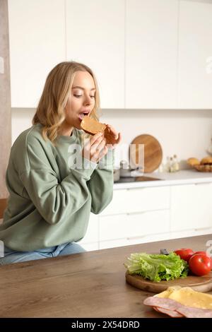 Giovane bella donna che mangia un gustoso toast con burro di arachidi in cucina Foto Stock