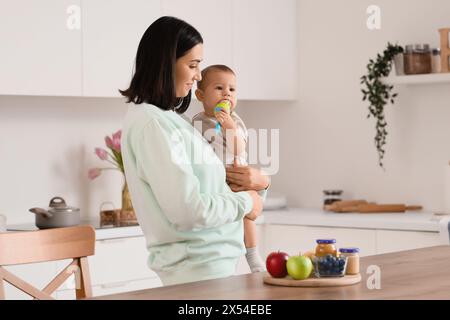 Madre che dà alla sua piccola rosticceria con il cibo in cucina Foto Stock