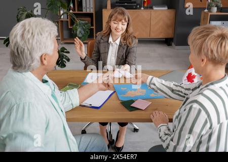 Agente di viaggio donna che dà biglietti per coppie mature al tavolo in ufficio Foto Stock