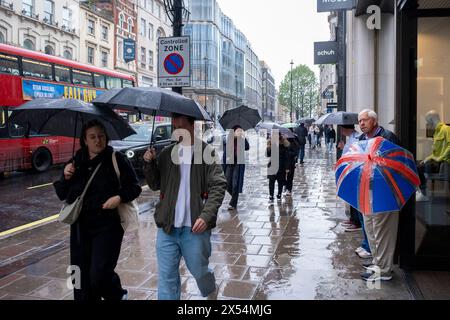 La pioggia del lunedì festivo non scoraggia i numerosi acquirenti e visitatori di Oxford Street che affrontano il maltempo usando gli ombrelli Union Flag il 6 maggio 2024 a Londra, Regno Unito. Oxford Street è un importante centro commerciale nel West End della capitale ed è la strada commerciale più trafficata d'Europa, con circa mezzo milione di visitatori al giorno ai suoi circa 300 negozi, la maggior parte dei quali sono negozi di moda e di abbigliamento di alta moda. Foto Stock