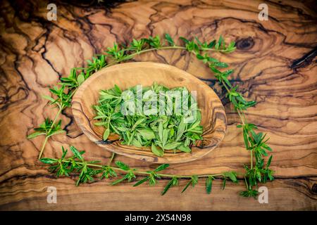Salato estivo, calamint (Satureja hortensis), schiacciato su un piatto di legno Foto Stock