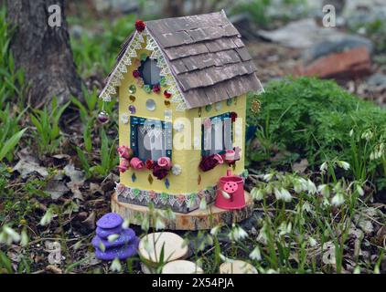 Graziosa casa di bambole con fiori primaverili all'aperto in giardino. Graziosa miniatura per biglietti d'auguri, nozze o compleanni, immobili, downsi Foto Stock