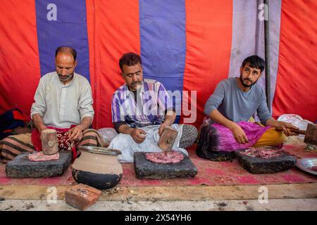 Gli chef Kashmiri stanno tritando il montone per preparare Wazwan durante una cerimonia nuziale a Srinagar. Wazwan è un tradizionale pasto Kashmiri a più portate, comunemente servito in occasione di matrimoni e altri eventi celebrativi. Include decine di pasti, che vanno da Rista e Rogan Josh a Kebabs cucinati principalmente con agnello. Wazwan è considerata una forma d'arte e una fonte di orgoglio per la cultura e l'identità kashmiri. Quasi tutte le ricette sono a base di carne, impiegando agnello o pollo, con alcuni piatti vegetariani. È ampiamente popolare in Kashmir e in tutto il mondo. Foto Stock