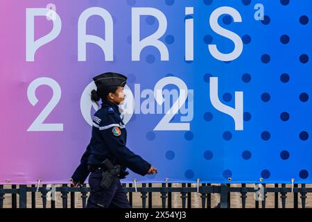 6 maggio 2024, Francia, Parigi: Una poliziotta passa davanti a uno striscione con le parole Paris 2024 davanti all'Assemblea Nazionale. Le Olimpiadi e le Paralimpiadi si svolgeranno in Francia quest'estate. Foto: Robert Michael/dpa Foto Stock
