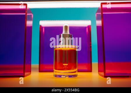 olio per viso giallo in flacone di vetro con contagocce su sfondo giallo e blu con elementi geometrici rosa e viola e luce al neon. Minimali vivaci e divertenti Foto Stock