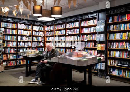 Un uomo maturo seduto su una sedia che guarda il suo smartphone all'interno di una libreria Waterstones nel centro di Truro in Cornovaglia, nel Regno Unito. Foto Stock