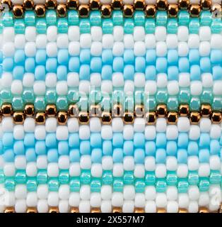 Foto macro dello sfondo con perline in stile boho. Motivo a righe con perline di colore bianco, blu e bronzo. Foto Stock