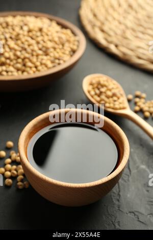 Gustosa salsa di soia nel recipiente e semi di soia sul tavolo nero, primo piano Foto Stock