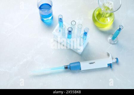 Analisi di laboratorio. Micropipetta e vetreria diversa con liquidi su tavolo in marmo grigio chiaro, vista dall'alto Foto Stock