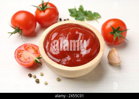 Delizioso ketchup nel recipiente, aglio e pomodori su un tavolo di legno bianco, primo piano Foto Stock