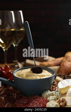 Fonduta con gustoso formaggio fuso, forchetta, diversi spuntini e vino in tavola Foto Stock