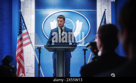 Giovane rappresentante dell'organizzazione che risponde alle domande dei giornalisti alla conferenza stampa. Addetto stampa che lavora alla riunione del Summit. Ministro che parla al Congresso. Sfondo con bandiere americane. Foto Stock