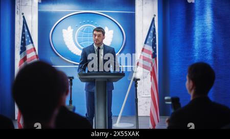 Giovane rappresentante dell'organizzazione che risponde alle domande dei giornalisti alla conferenza stampa. Addetto stampa che lavora alla riunione del Summit. Ministro che parla al Congresso. Sfondo con bandiere americane. Foto Stock