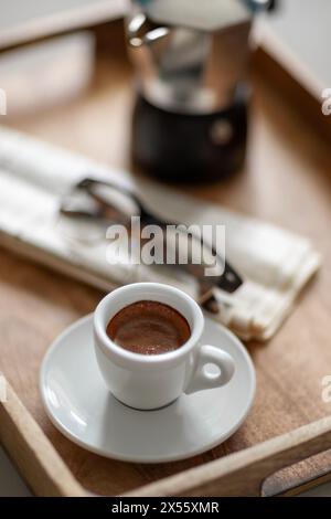 Espresso fresco in una tazza bianca su un vassoio di legno accanto ai bicchieri da lettura e al quotidiano Foto Stock