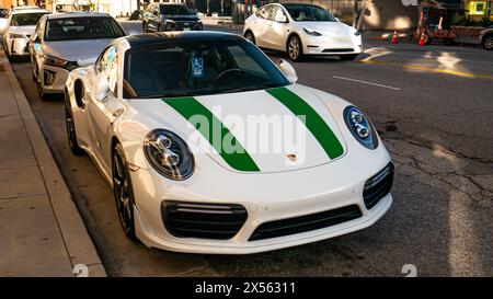 Un'elegante Porsche 911 bianca con strisce verdi da corsa e un cartello per disabili parcheggiata su una strada della città, circondata da altre auto moderne in una giornata di sole Foto Stock