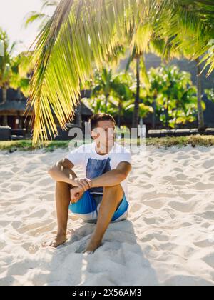 Un ragazzo giovane che si rilassa e si siede sulla spiaggia. Vacanza da uomo sottile sulla spiaggia paradisiaca Foto Stock