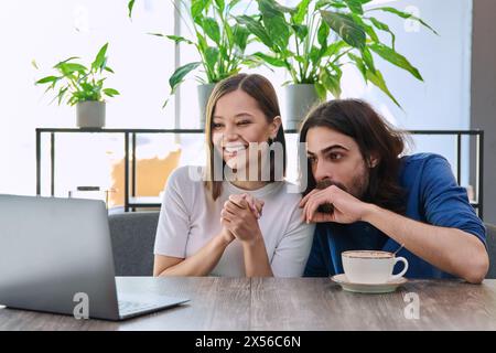 Felice sorprese una giovane coppia che guardava insieme un notebook mentre era seduta in una caffetteria Foto Stock