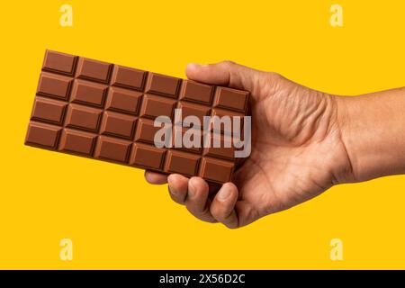 Mano di un uomo irriconoscibile che regge una barretta di cioccolato su sfondo giallo Foto Stock