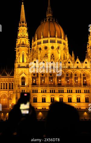 Un turista cerca di catturare con il suo telefono la vista notturna dell'edificio illuminato del Parlamento ungherese, a Budapest. Foto Stock