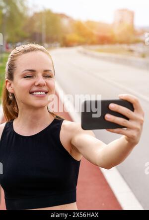 Una donna bruna che indossa un abbigliamento sportivo scatta un selfie mentre corre in pista in città. Foto Stock