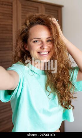 La bella bruna riccia fa selfie usando il suo telefono. Una donna condivide la sua foto sui social network... Foto Stock