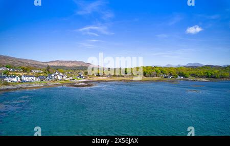 Arisaig Lochaber Scozia piccola baia mare turchese e fila di case su una costa rocciosa con alberi in primavera Foto Stock