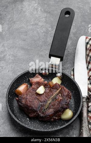 Bistecca di manzo fritta con erbe aromatiche in padella piccola su sfondo grigio Foto Stock