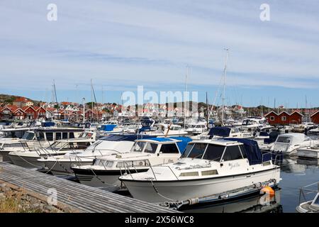 Skärhamn, Svezia - 13 luglio 2022: Molte barche a motore e a vela ormeggiate al porto. Case e capanne di un villaggio costiero di pescatori sullo sfondo. Nessuna piuma visibile Foto Stock