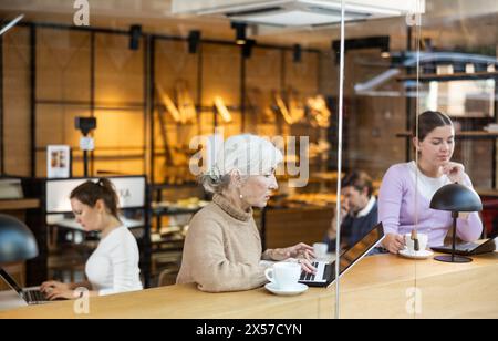 Una vecchia donna europea che beve e si diverte a bere e a gustare il caffè mentre lavora sul computer portatile nel bar Foto Stock
