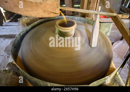 Una mola sta girando. Una pietra macina il grano in un mulino. Produzione di farina di mais. I chicchi di mais cadono nel mulino. Tradizionale mulino ad acqua sul fiume Foto Stock