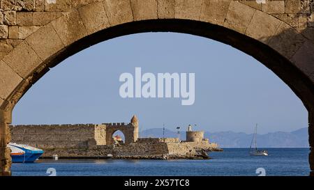 Ammira il mare attraverso un arco con finestra in pietra e un piccolo castello sullo sfondo, la Torre De Naillac, il forte di San Nicola, la zona del porto, Rodi Foto Stock